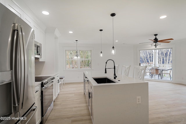 kitchen with white cabinets, appliances with stainless steel finishes, a kitchen island with sink, light countertops, and a sink