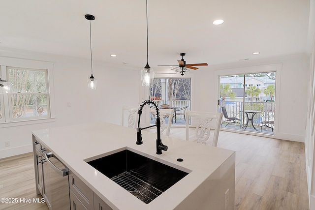 kitchen featuring light wood finished floors, pendant lighting, light countertops, and a sink