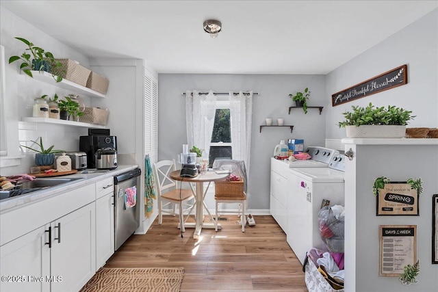 interior space featuring washer and clothes dryer, open shelves, stainless steel dishwasher, light wood-style floors, and white cabinetry