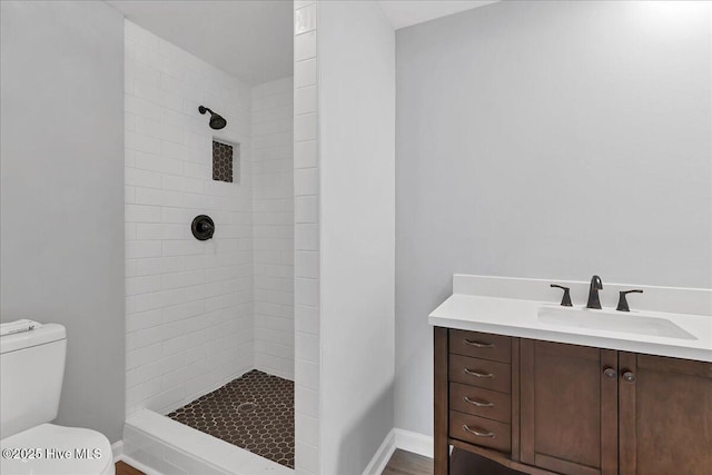 full bathroom with toilet, baseboards, tiled shower, and vanity