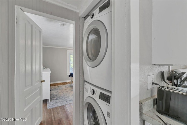 washroom with laundry area, ornamental molding, stacked washer / dryer, and light wood-type flooring