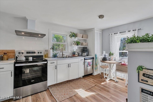 kitchen featuring appliances with stainless steel finishes, white cabinets, light countertops, and wall chimney range hood