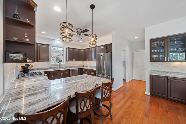 kitchen with stainless steel appliances, light wood-style floors, light stone countertops, dark brown cabinets, and ceiling fan