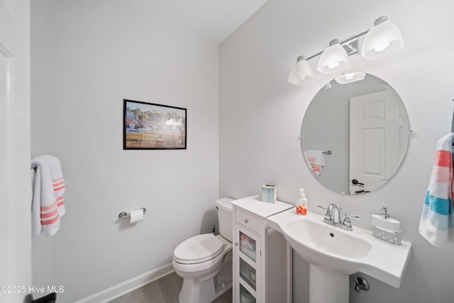 bathroom featuring toilet, wood finished floors, baseboards, and a sink