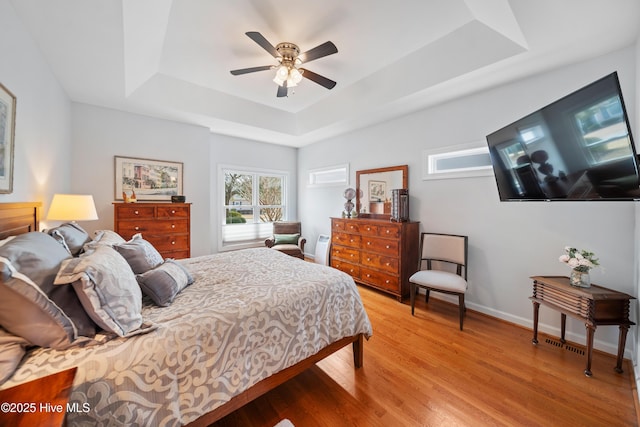 bedroom featuring ceiling fan, baseboards, light wood-style floors, and a tray ceiling