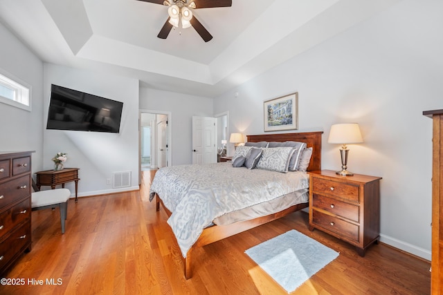 bedroom with a raised ceiling, light wood-style floors, visible vents, and baseboards