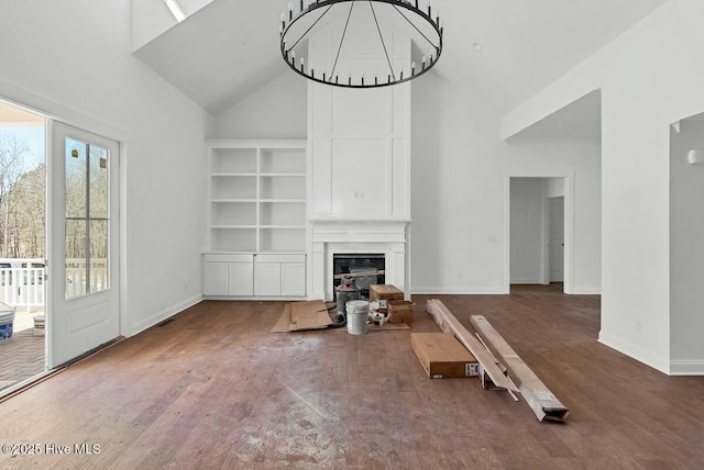 unfurnished living room featuring high vaulted ceiling, a glass covered fireplace, an inviting chandelier, and wood finished floors