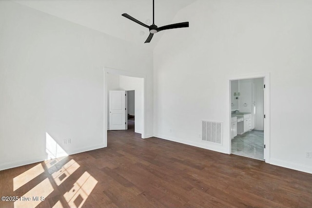 unfurnished bedroom featuring dark wood-style flooring, visible vents, a towering ceiling, and baseboards