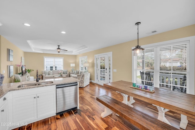 kitchen featuring a sink, visible vents, dishwasher, a tray ceiling, and dark wood finished floors