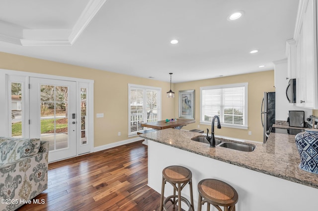 kitchen featuring stainless steel appliances, white cabinets, a sink, light stone countertops, and a peninsula