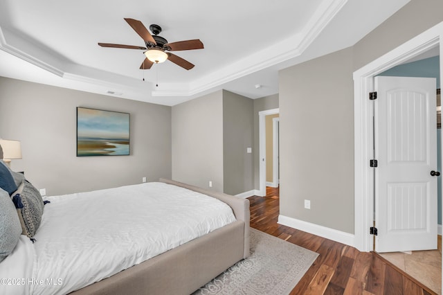 bedroom featuring ceiling fan, a tray ceiling, wood finished floors, and baseboards