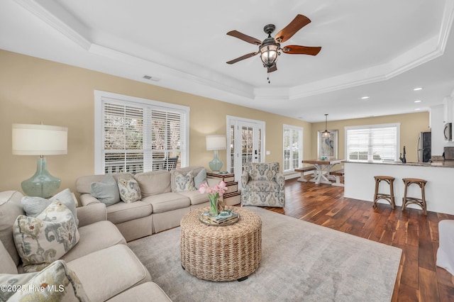 living area featuring ceiling fan, recessed lighting, dark wood-type flooring, visible vents, and a raised ceiling