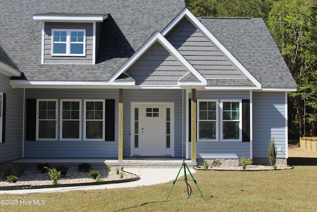 view of front of house featuring a front yard, a shingled roof, and covered porch