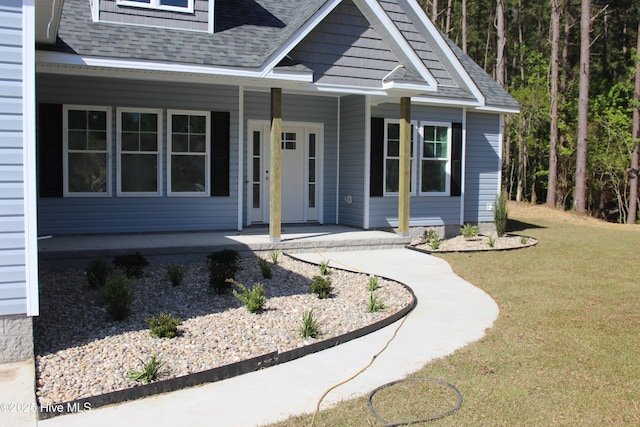 view of front of home with covered porch, a front yard, and roof with shingles