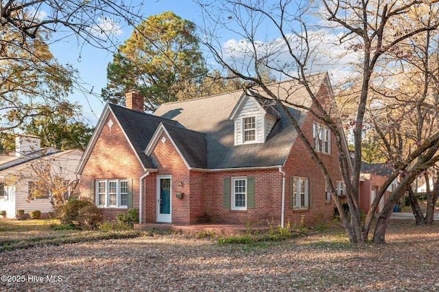 view of front facade with a shingled roof, brick siding, and a chimney