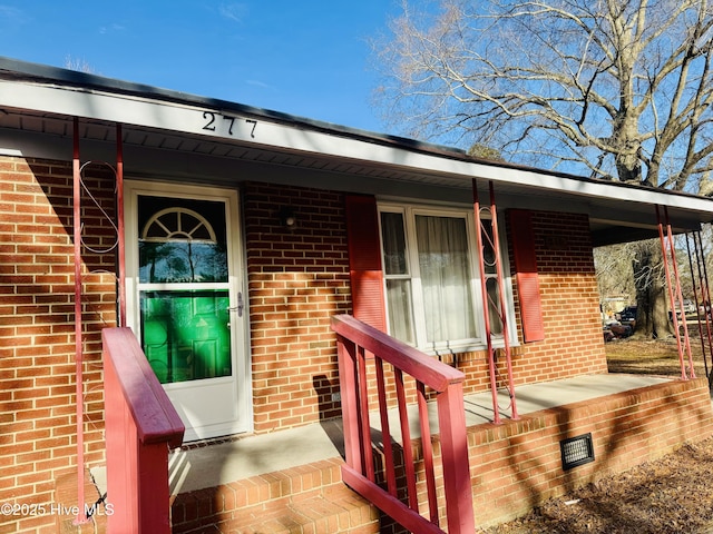 doorway to property with crawl space, covered porch, and brick siding