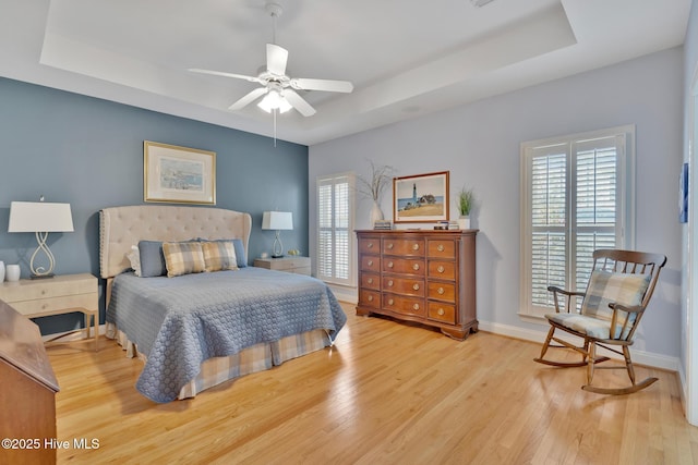 bedroom with light wood-style floors, a tray ceiling, and multiple windows