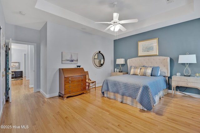 bedroom with a raised ceiling, ceiling fan, baseboards, and wood finished floors