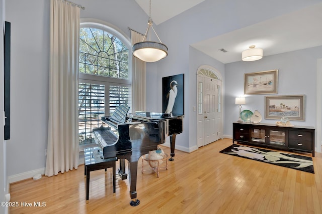 living area featuring light wood-style floors, visible vents, high vaulted ceiling, and baseboards