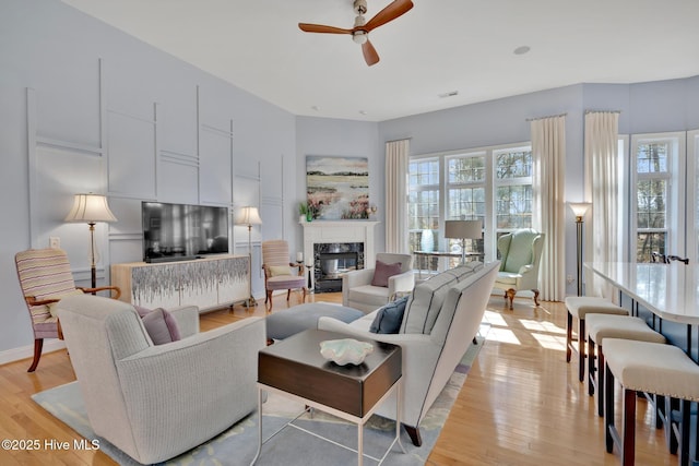 living area featuring light wood-type flooring, a premium fireplace, baseboards, and a ceiling fan