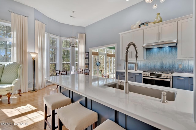 kitchen featuring a chandelier, under cabinet range hood, a breakfast bar, hanging light fixtures, and gas range