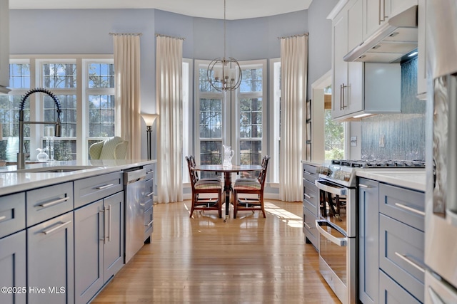 kitchen featuring appliances with stainless steel finishes, hanging light fixtures, light countertops, under cabinet range hood, and a sink