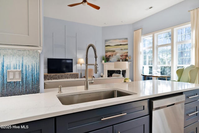 kitchen with open floor plan, light stone countertops, gray cabinetry, stainless steel dishwasher, and a sink