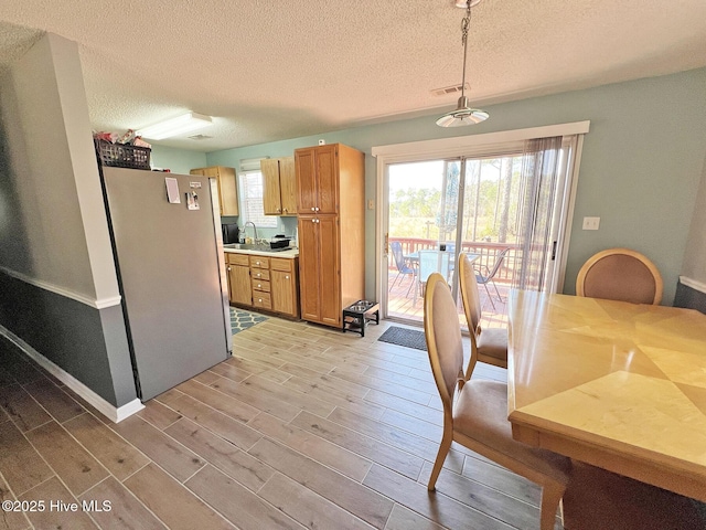 kitchen featuring a sink, hanging light fixtures, light countertops, freestanding refrigerator, and wood tiled floor