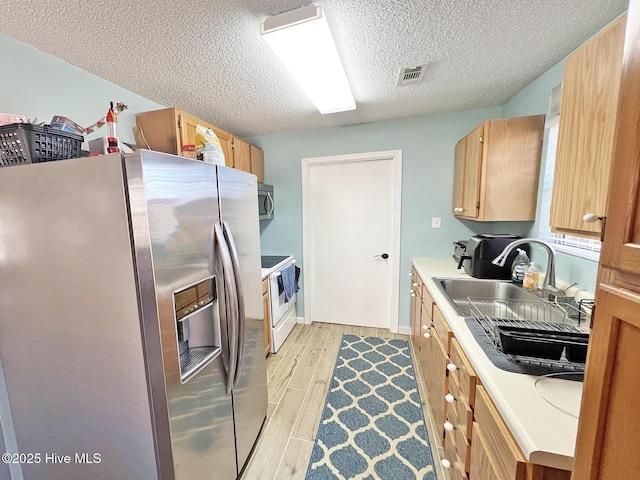 kitchen with appliances with stainless steel finishes, light countertops, light wood-style floors, and visible vents