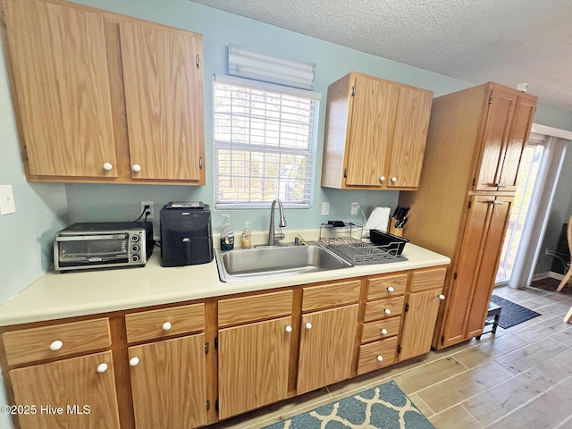 kitchen with a toaster, light countertops, a textured ceiling, wood finish floors, and a sink