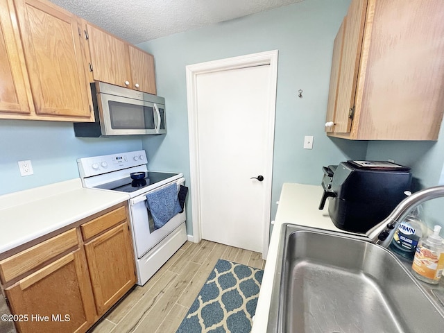 kitchen with white electric stove, light countertops, stainless steel microwave, a sink, and light wood-type flooring