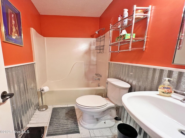 bathroom featuring toilet, a wainscoted wall, a textured ceiling, washtub / shower combination, and a sink