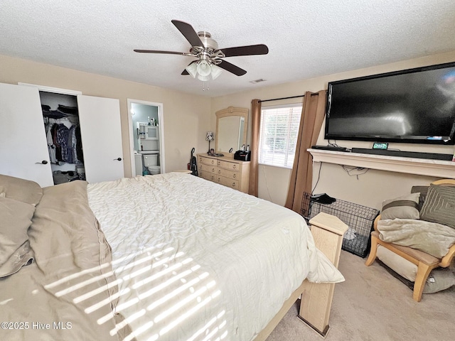 bedroom featuring a textured ceiling, ceiling fan, ensuite bathroom, light colored carpet, and a spacious closet