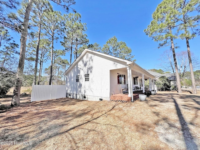 view of side of property with covered porch, crawl space, and fence