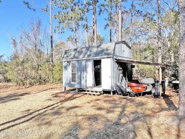 view of outbuilding featuring dirt driveway, a carport, and an outdoor structure