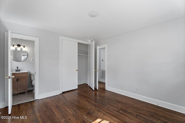 unfurnished bedroom featuring a sink, a closet, dark wood finished floors, and baseboards