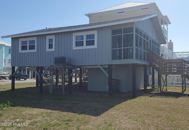 back of house with central air condition unit, a shingled roof, a sunroom, stairs, and a yard