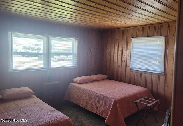 bedroom with dark colored carpet, wooden ceiling, and wood walls