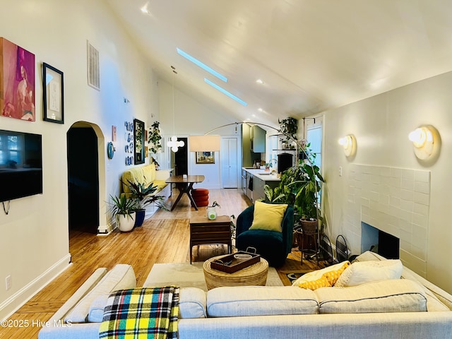 living room featuring arched walkways, a brick fireplace, visible vents, and light wood finished floors