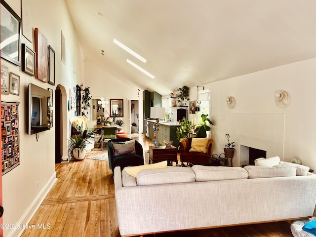 living room featuring vaulted ceiling, light wood finished floors, arched walkways, and baseboards