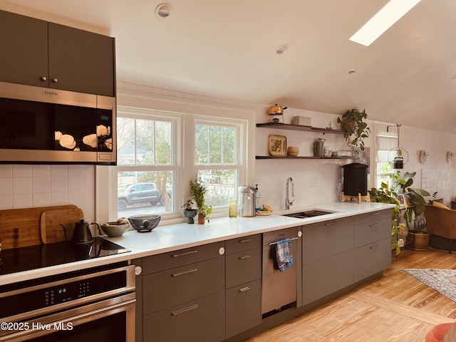 kitchen featuring stainless steel appliances, a sink, light wood-style floors, light countertops, and backsplash