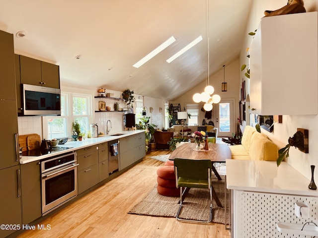 kitchen with a sink, light countertops, appliances with stainless steel finishes, light wood-type flooring, and pendant lighting