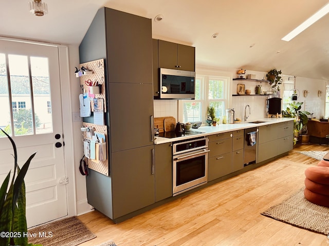 kitchen with a sink, light countertops, black appliances, light wood finished floors, and tasteful backsplash