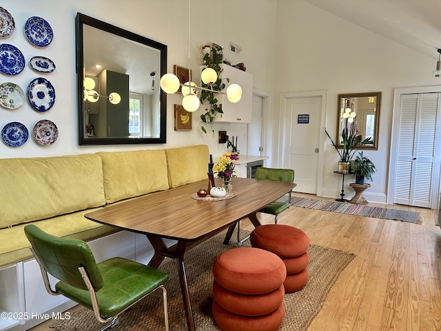 dining space with breakfast area, visible vents, wood finished floors, high vaulted ceiling, and baseboards