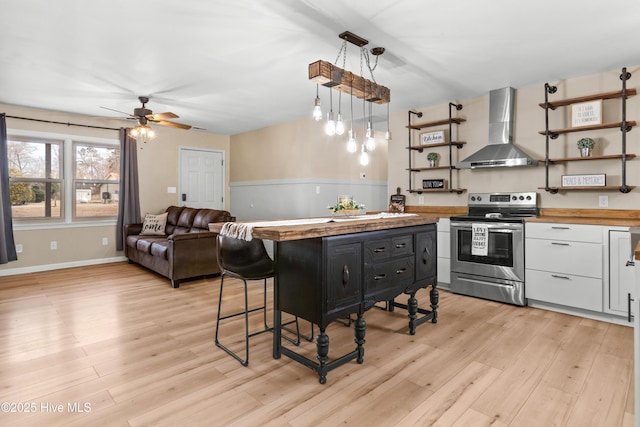 kitchen featuring wall chimney range hood, butcher block countertops, stainless steel range with electric stovetop, white cabinets, and open shelves