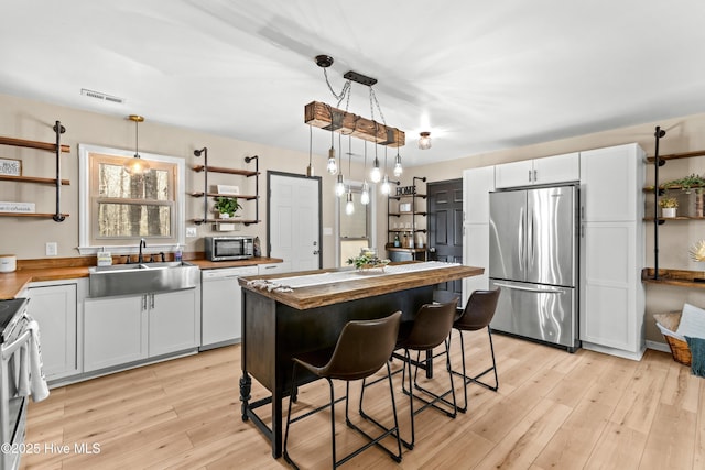 kitchen with visible vents, open shelves, a sink, appliances with stainless steel finishes, and butcher block counters