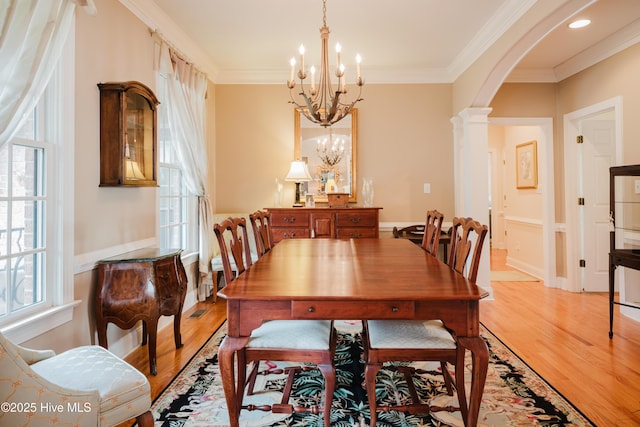 dining room with light wood-style flooring, arched walkways, a chandelier, and ornamental molding