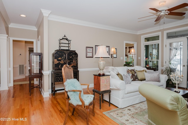 living area with light wood finished floors, baseboards, visible vents, a ceiling fan, and crown molding