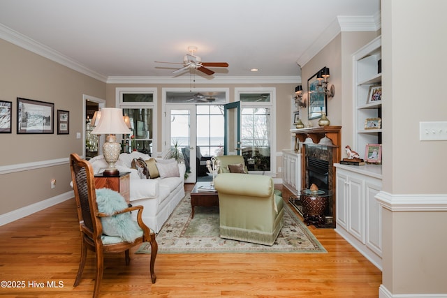 living room featuring baseboards, built in features, crown molding, light wood-type flooring, and a fireplace