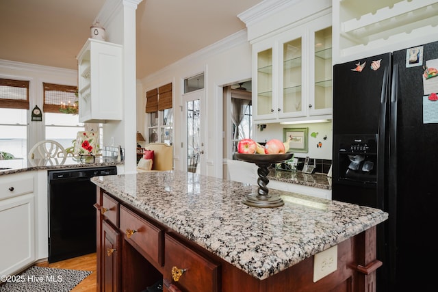 kitchen with a kitchen island, ornamental molding, light stone countertops, black appliances, and glass insert cabinets